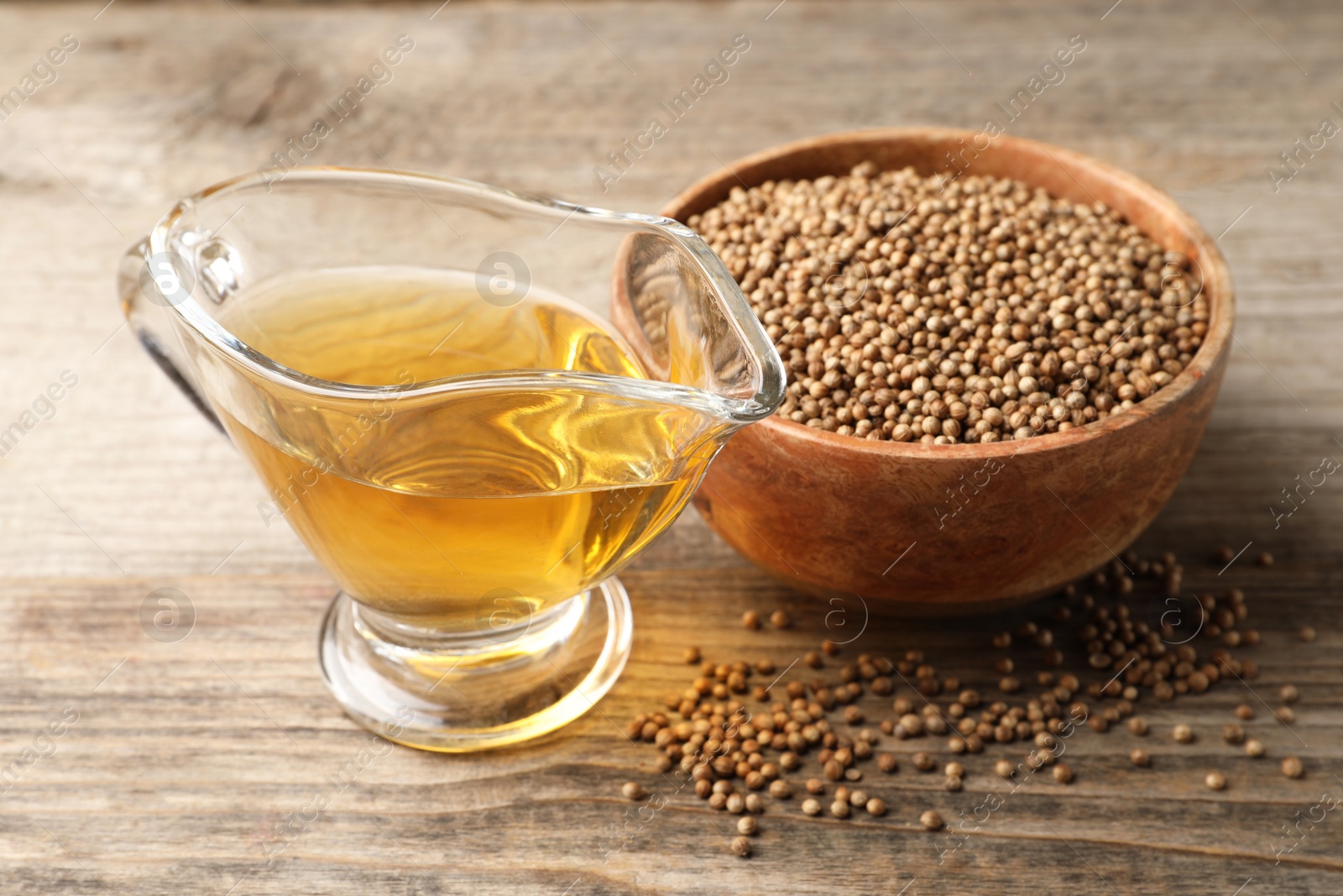 Photo of Dried coriander seeds in bowl and oil on wooden table