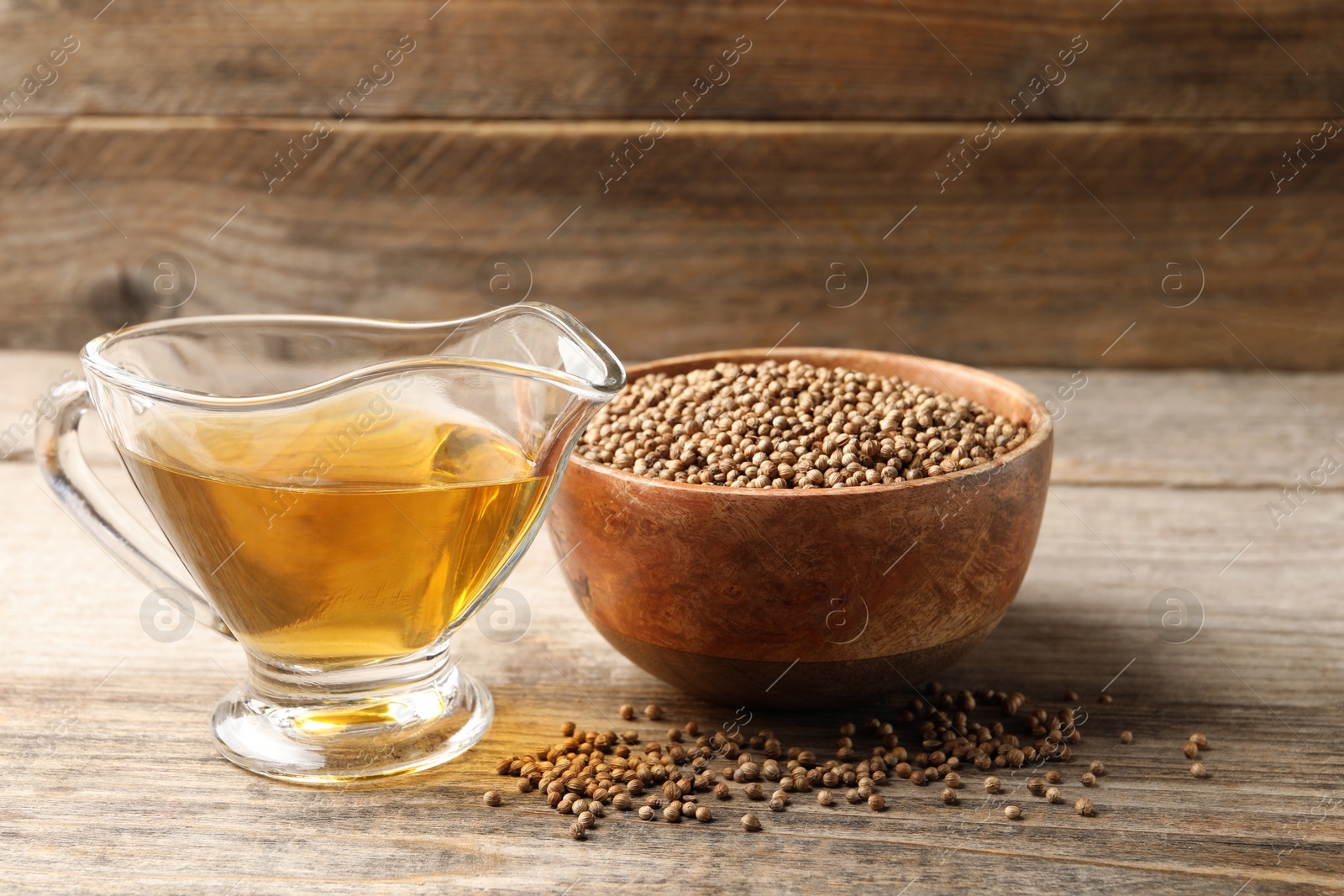 Photo of Dried coriander seeds in bowl and oil on wooden table