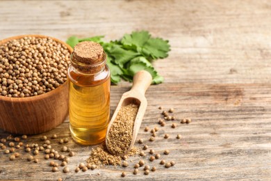 Photo of Coriander essential oil, powder, seeds and green leaves on wooden table, space for text