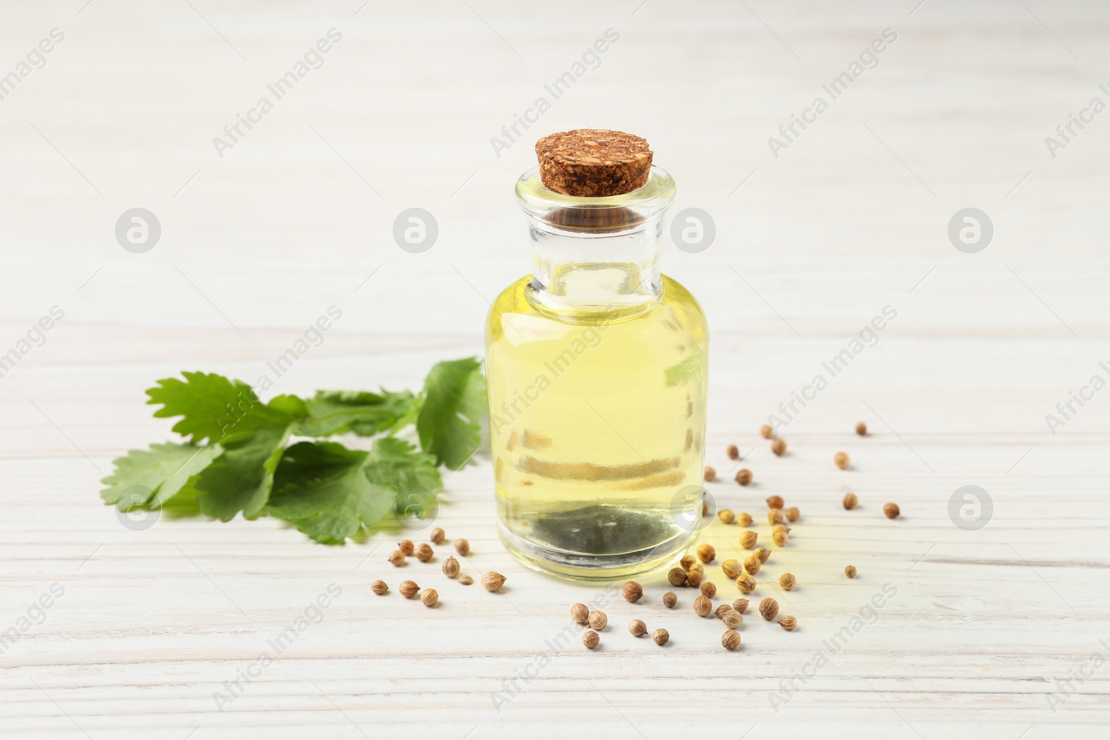 Photo of Coriander essential oil, seeds and green leaves on wooden table