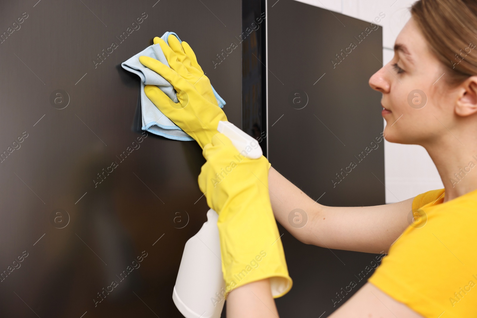 Photo of Professional janitor wearing uniform cleaning fridge in kitchen, closeup