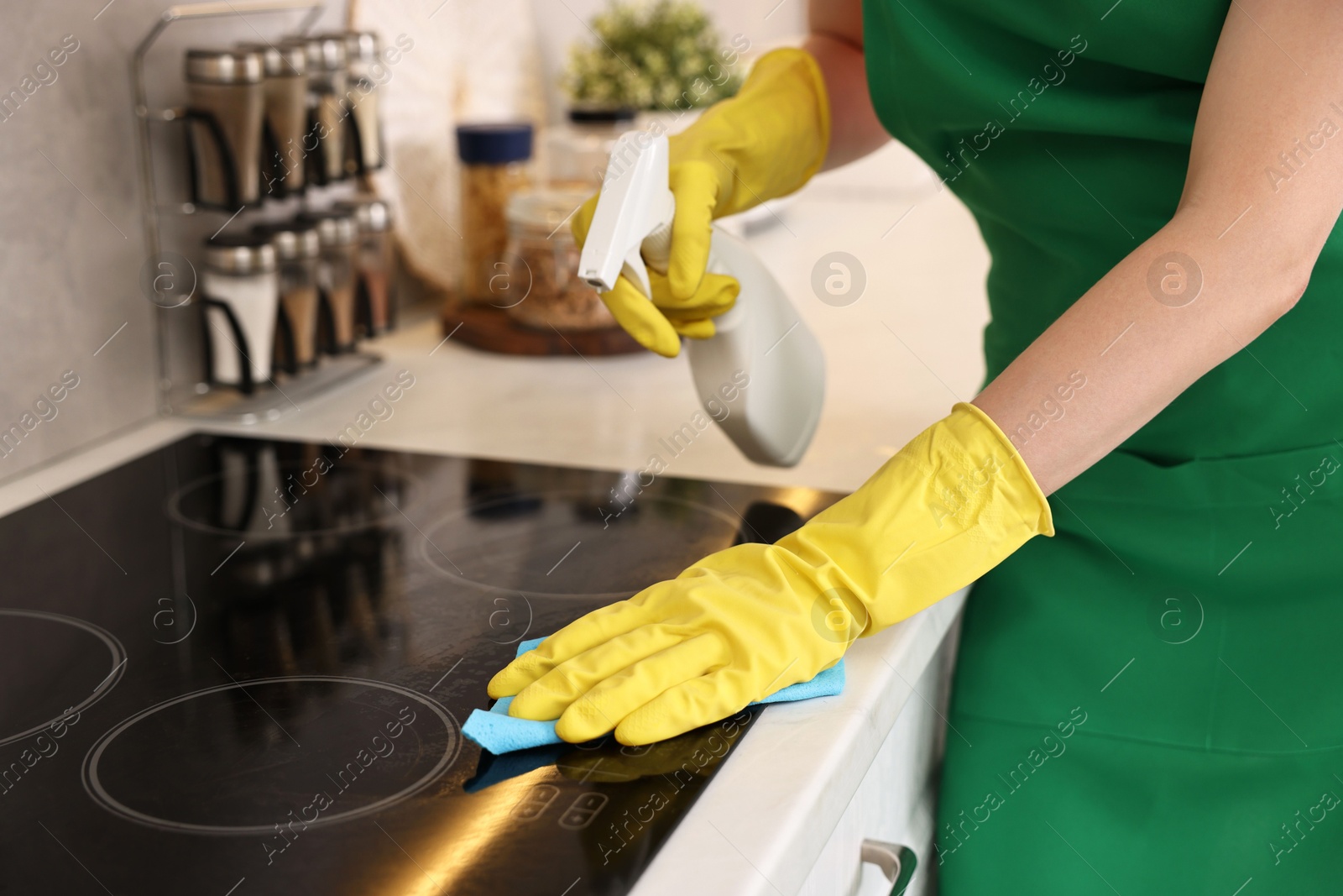 Photo of Professional janitor wearing uniform cleaning electric stove in kitchen, closeup