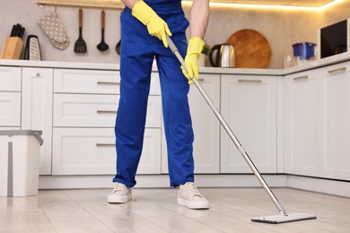 Photo of Cleaning service worker washing floor with mop in kitchen, closeup