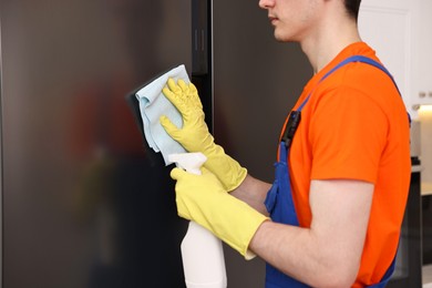 Photo of Professional janitor wearing uniform cleaning fridge in kitchen, closeup