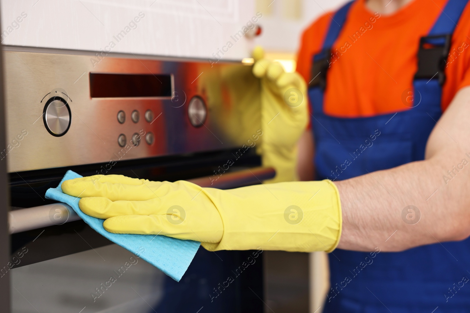 Photo of Professional janitor wearing uniform cleaning electric oven in kitchen, closeup