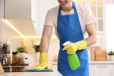 Professional janitor wearing uniform cleaning countertop in kitchen, closeup