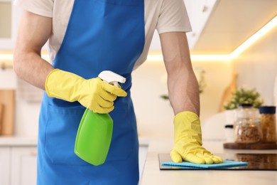 Professional janitor wearing uniform cleaning countertop in kitchen, closeup