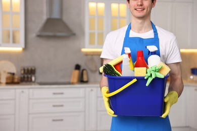 Photo of Cleaning service worker holding bucket with supplies in kitchen, closeup. Space for text