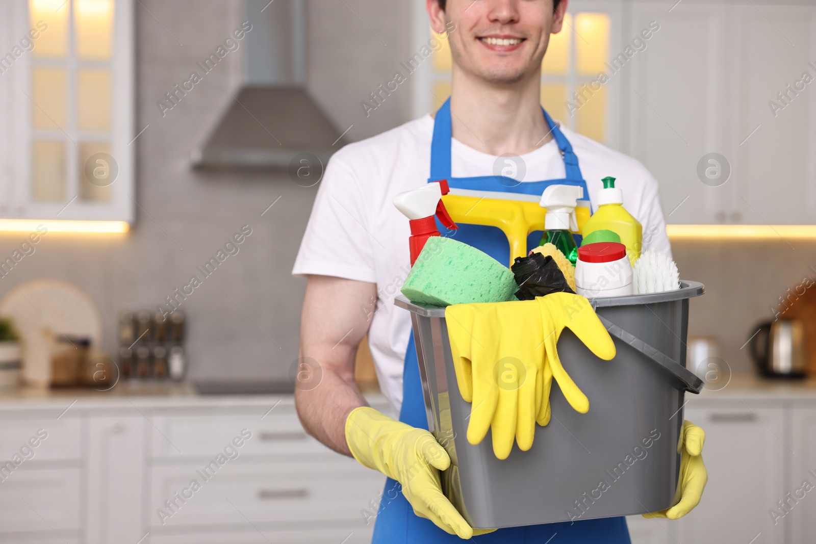 Photo of Cleaning service worker holding bucket with supplies in kitchen, closeup. Space for text