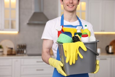 Cleaning service worker holding bucket with supplies in kitchen, closeup. Space for text