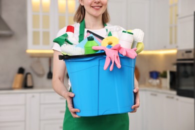 Photo of Cleaning service worker holding bucket with supplies in kitchen, closeup