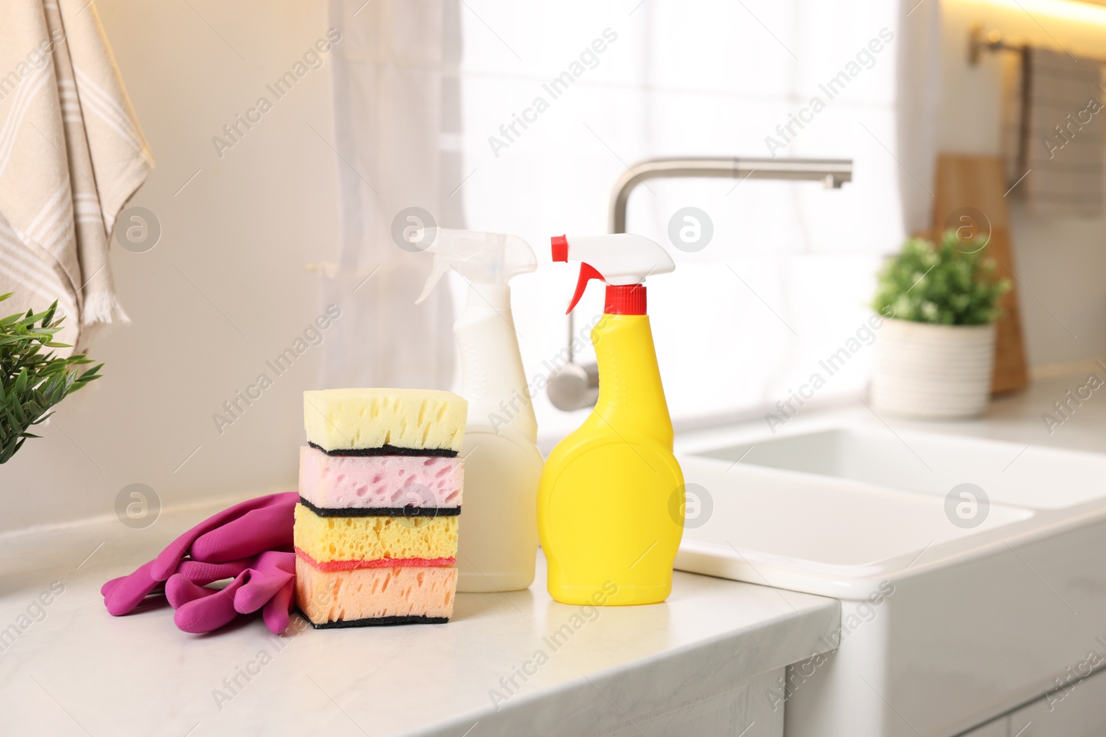 Photo of Cleaning service. Detergents, sponges and gloves on table in kitchen