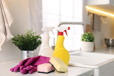 Photo of Cleaning service. Detergents, sponges and gloves on table in kitchen