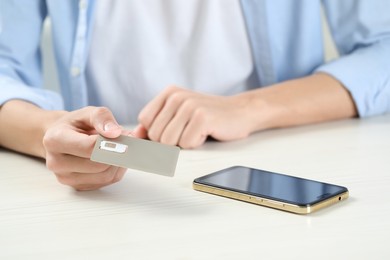 Photo of Man holding SIM card near smartphone at white wooden table, closeup