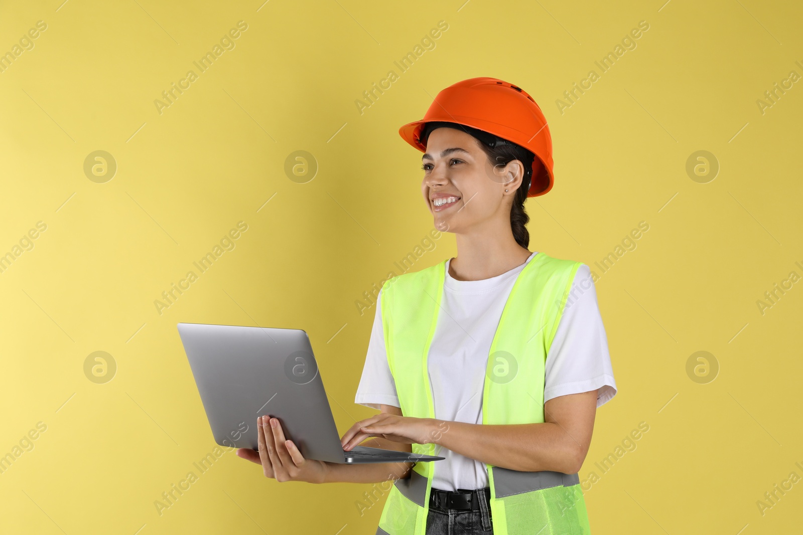 Photo of Engineer in hard hat with laptop on yellow background