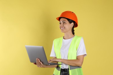 Engineer in hard hat with laptop on yellow background