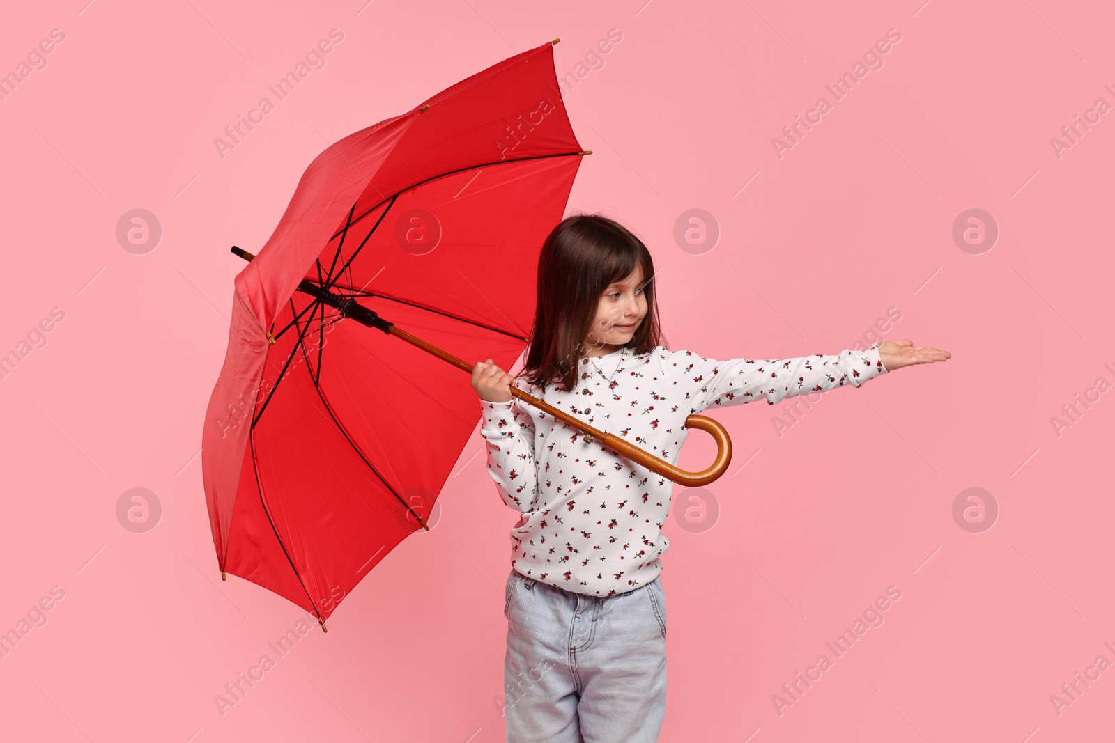 Photo of Cute little girl with red umbrella on pink background