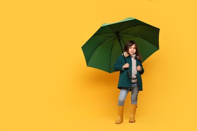 Photo of Cute little girl with green umbrella on yellow background. Space for text