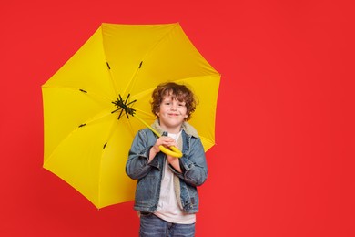 Photo of Little boy with yellow umbrella on red background, space for text