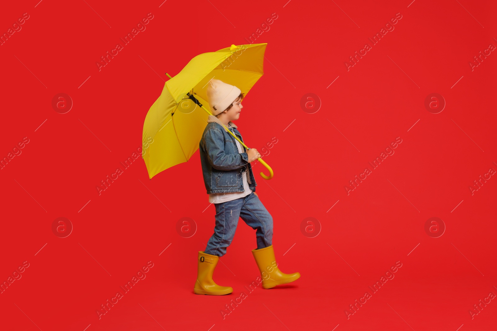 Photo of Little boy with yellow umbrella on red background, space for text