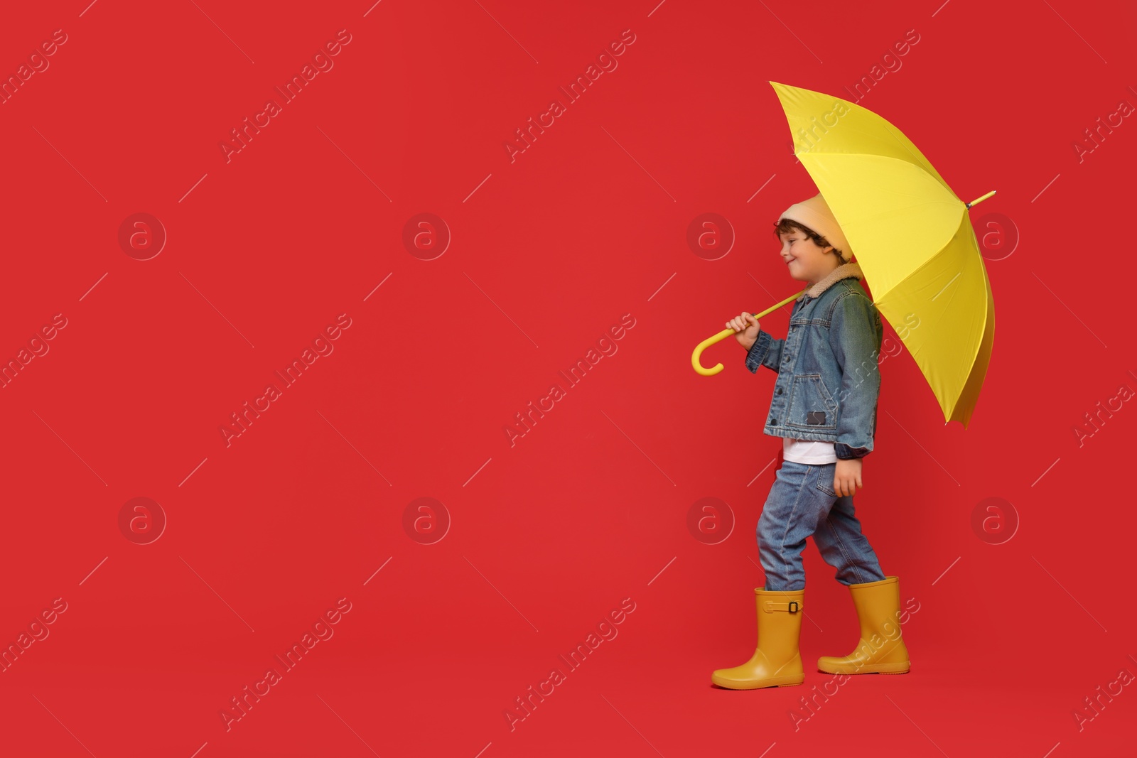 Photo of Little boy with yellow umbrella on red background, space for text