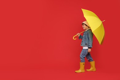 Photo of Little boy with yellow umbrella on red background, space for text