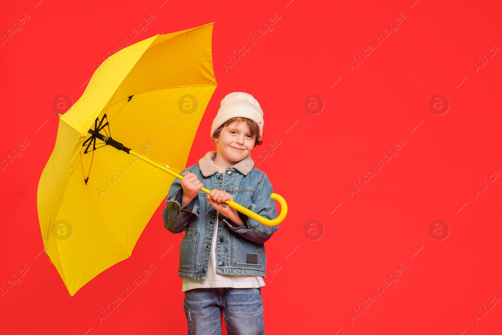 Photo of Little boy with yellow umbrella on red background, space for text