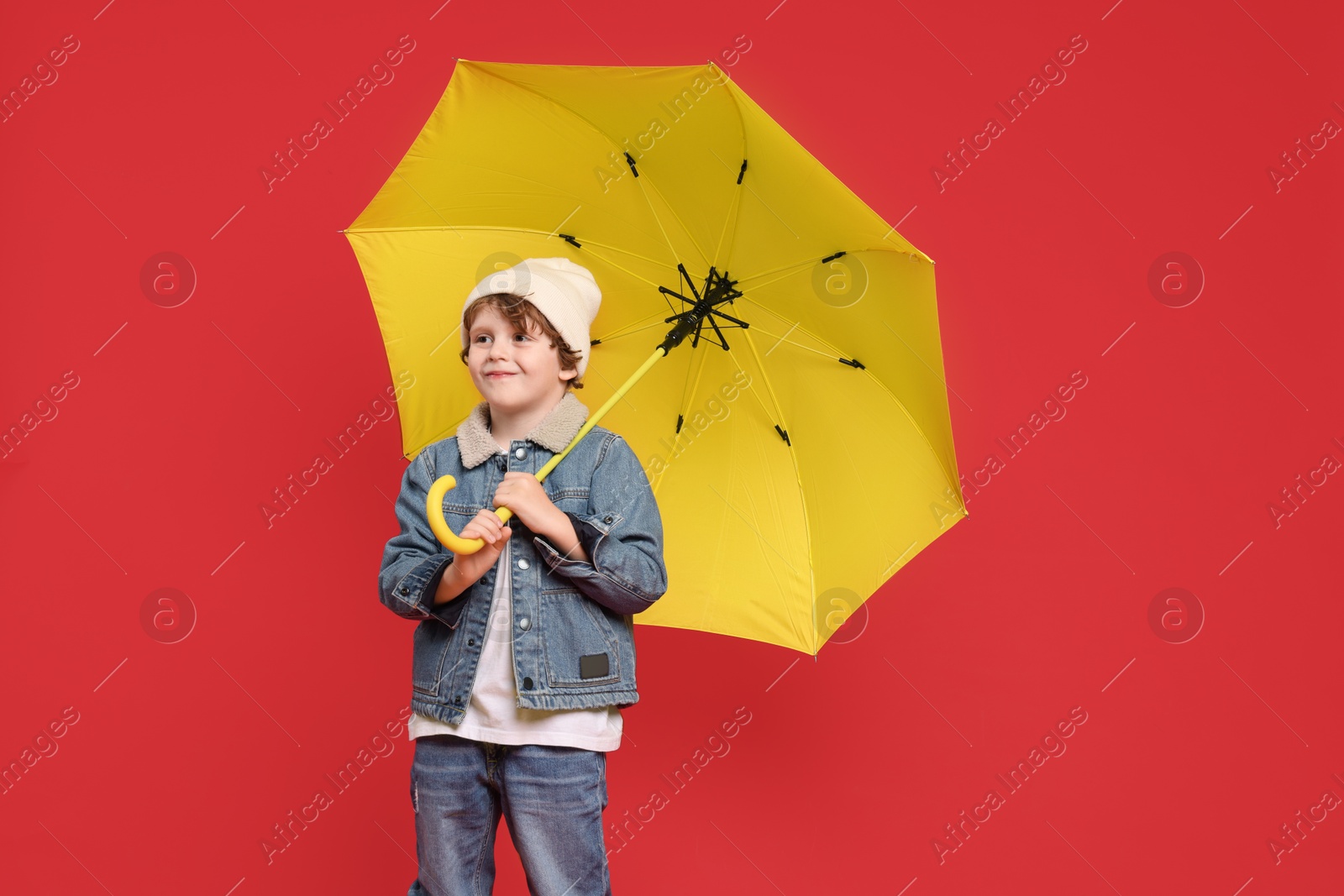 Photo of Little boy with yellow umbrella on red background