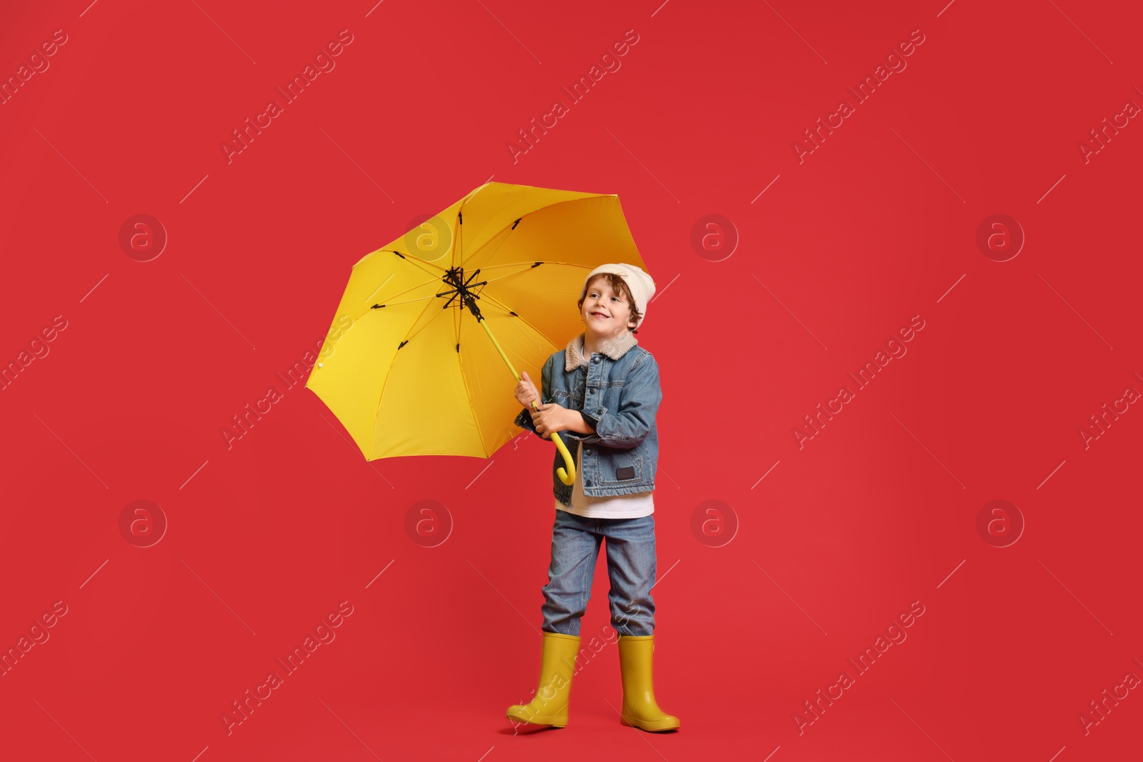 Photo of Little boy with yellow umbrella on red background, space for text