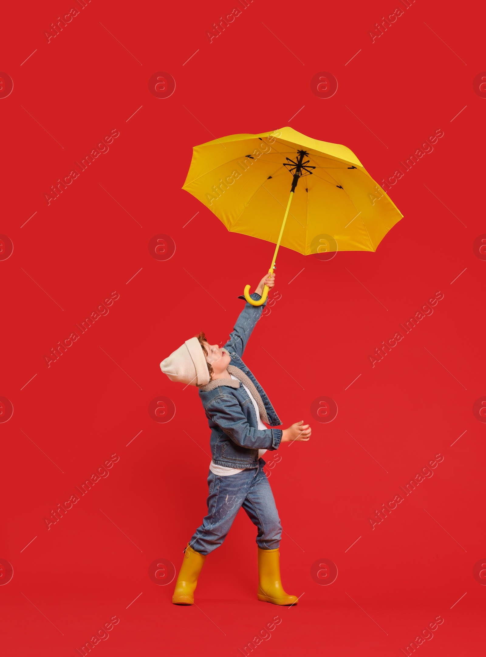 Photo of Little boy with yellow umbrella on red background, space for text