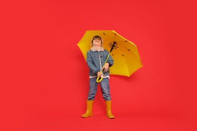 Photo of Little boy with yellow umbrella on red background
