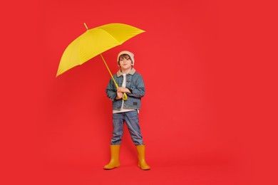 Little boy with yellow umbrella on red background, space for text