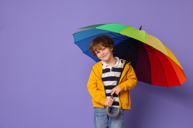 Little boy with rainbow umbrella on purple background, space for text