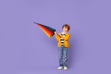 Little boy with rainbow umbrella on purple background