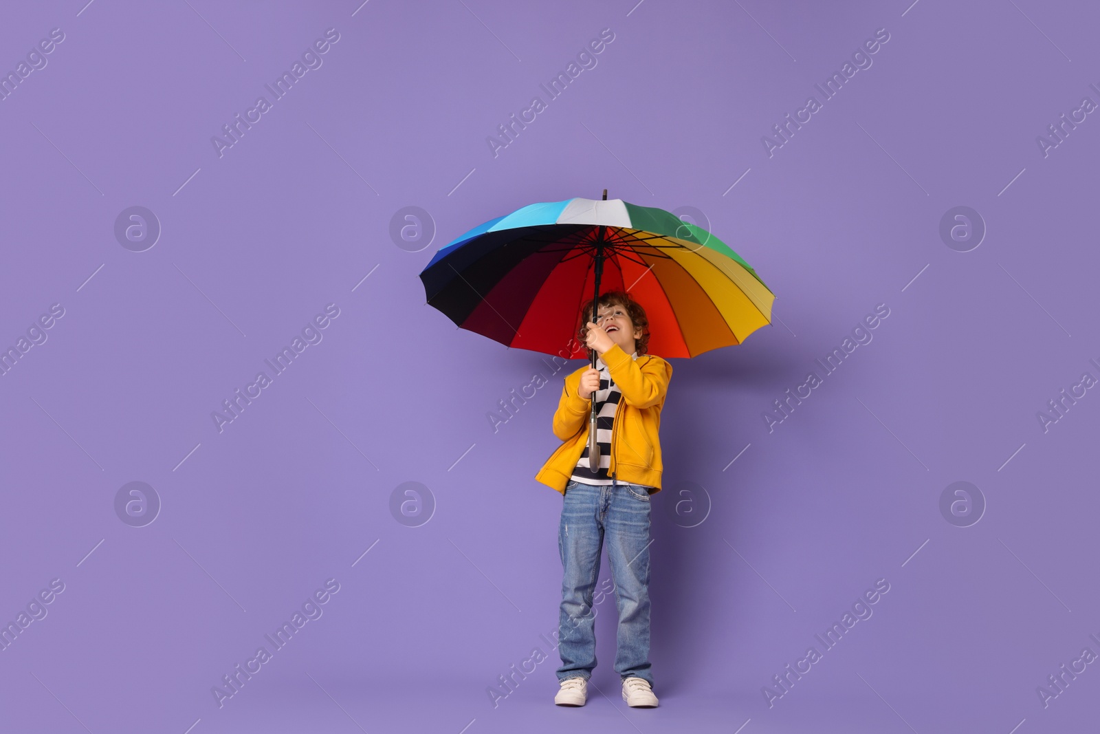 Photo of Little boy with rainbow umbrella on purple background