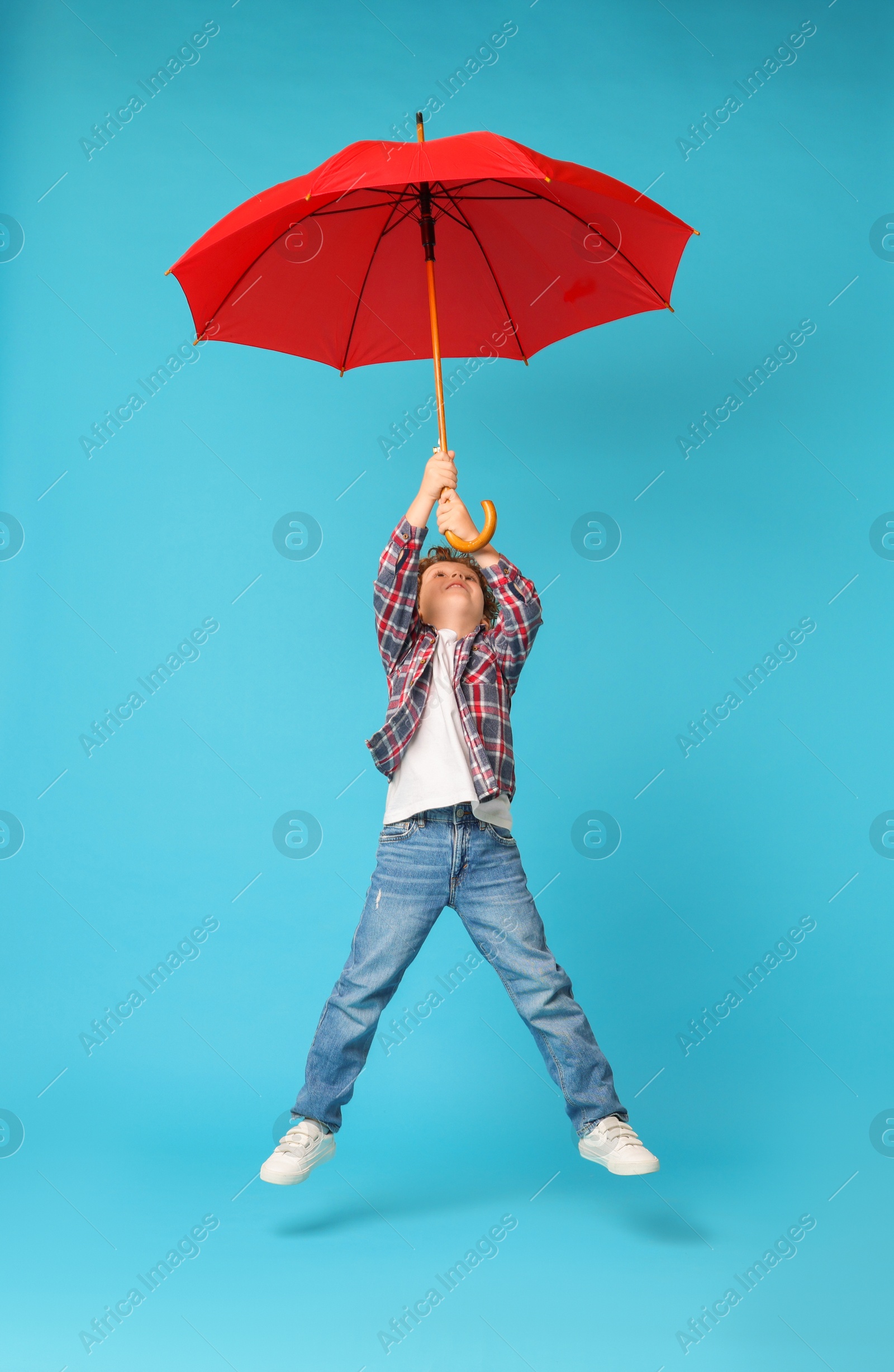 Photo of Little boy with red umbrella on light blue background