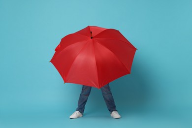 Little boy with red umbrella on light blue background