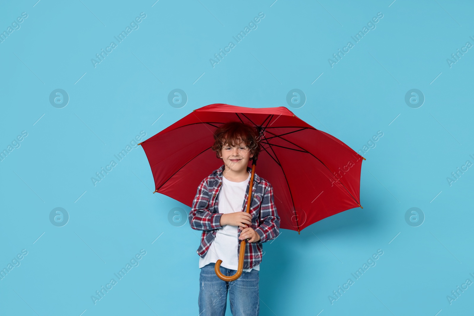 Photo of Little boy with red umbrella on light blue background, space for text