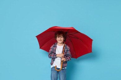 Little boy with red umbrella on light blue background, space for text