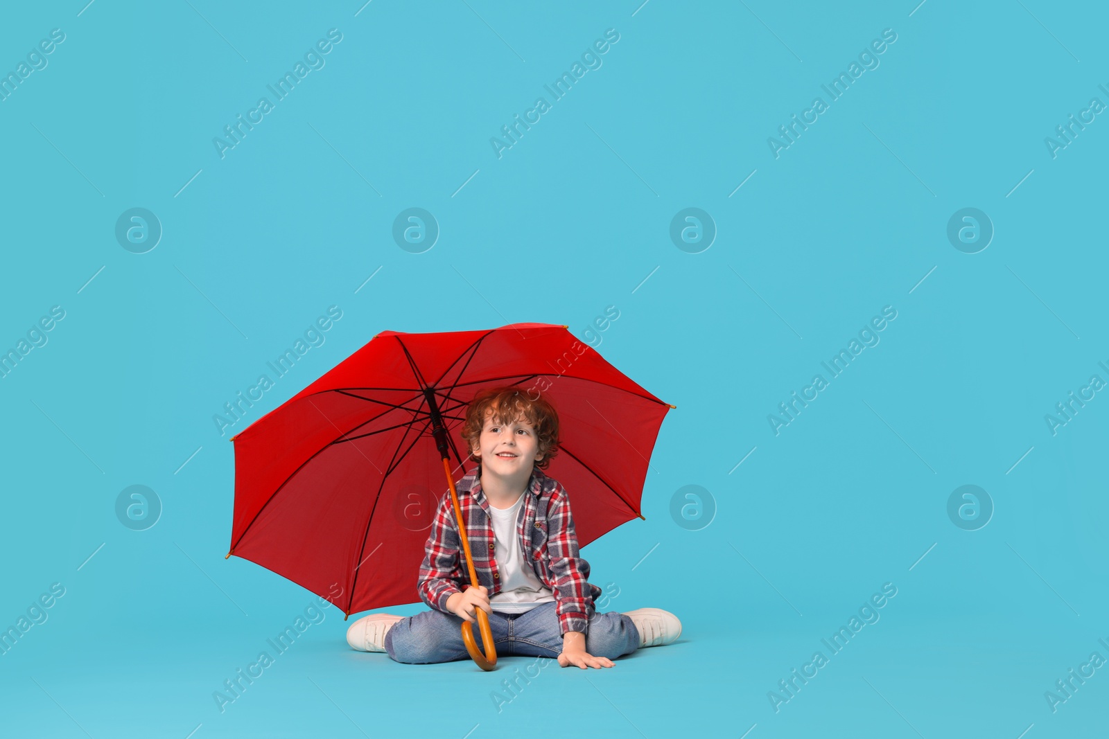 Photo of Little boy with red umbrella on light blue background, space for text