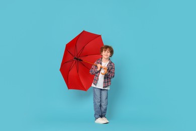 Photo of Little boy with red umbrella on light blue background, space for text