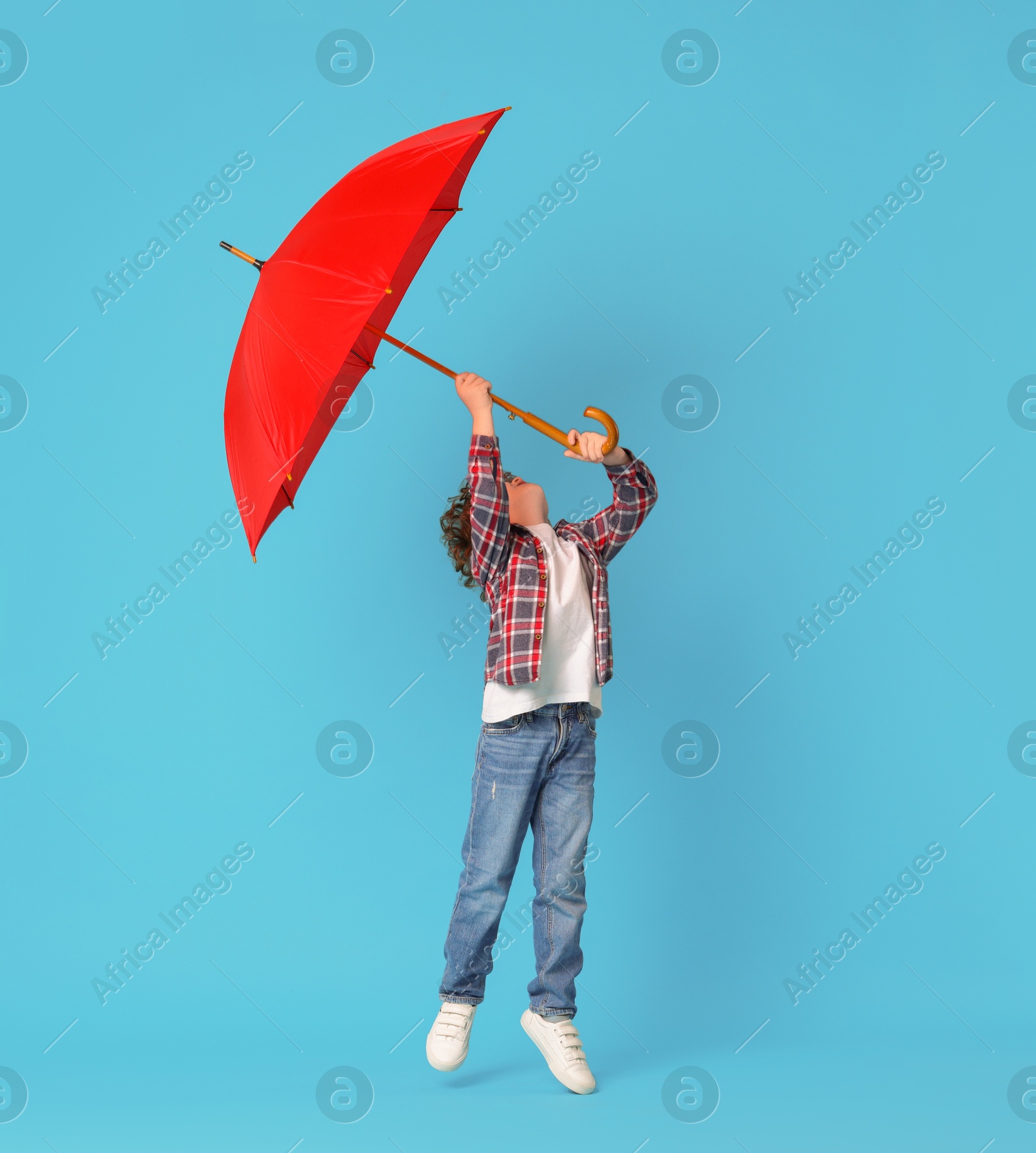 Photo of Little boy with red umbrella on light blue background