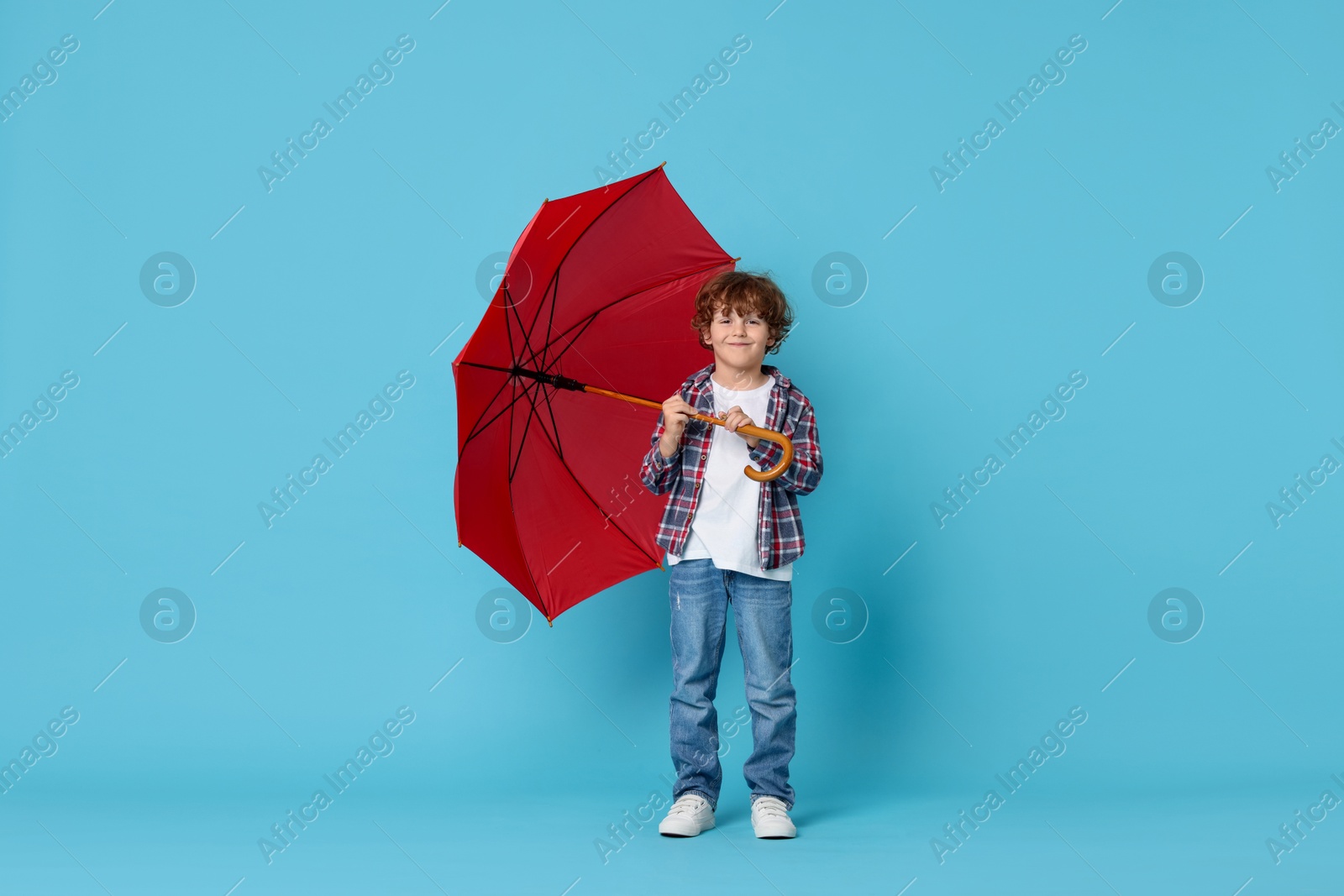 Photo of Little boy with red umbrella on light blue background