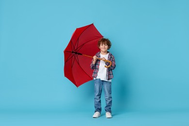 Little boy with red umbrella on light blue background