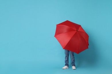 Little boy with red umbrella on light blue background, space for text