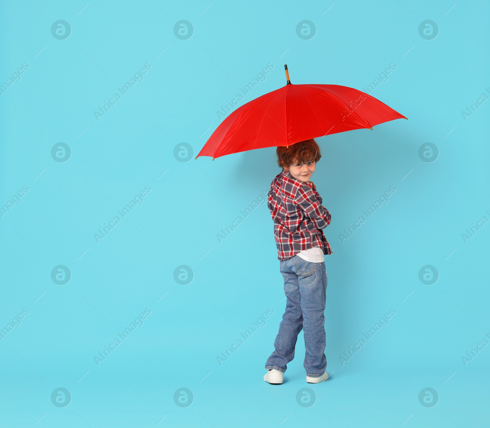 Photo of Little boy with red umbrella on light blue background, space for text