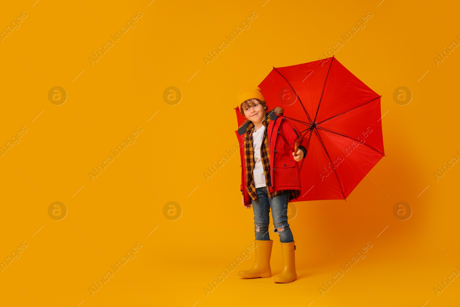 Photo of Little boy with red umbrella on orange background