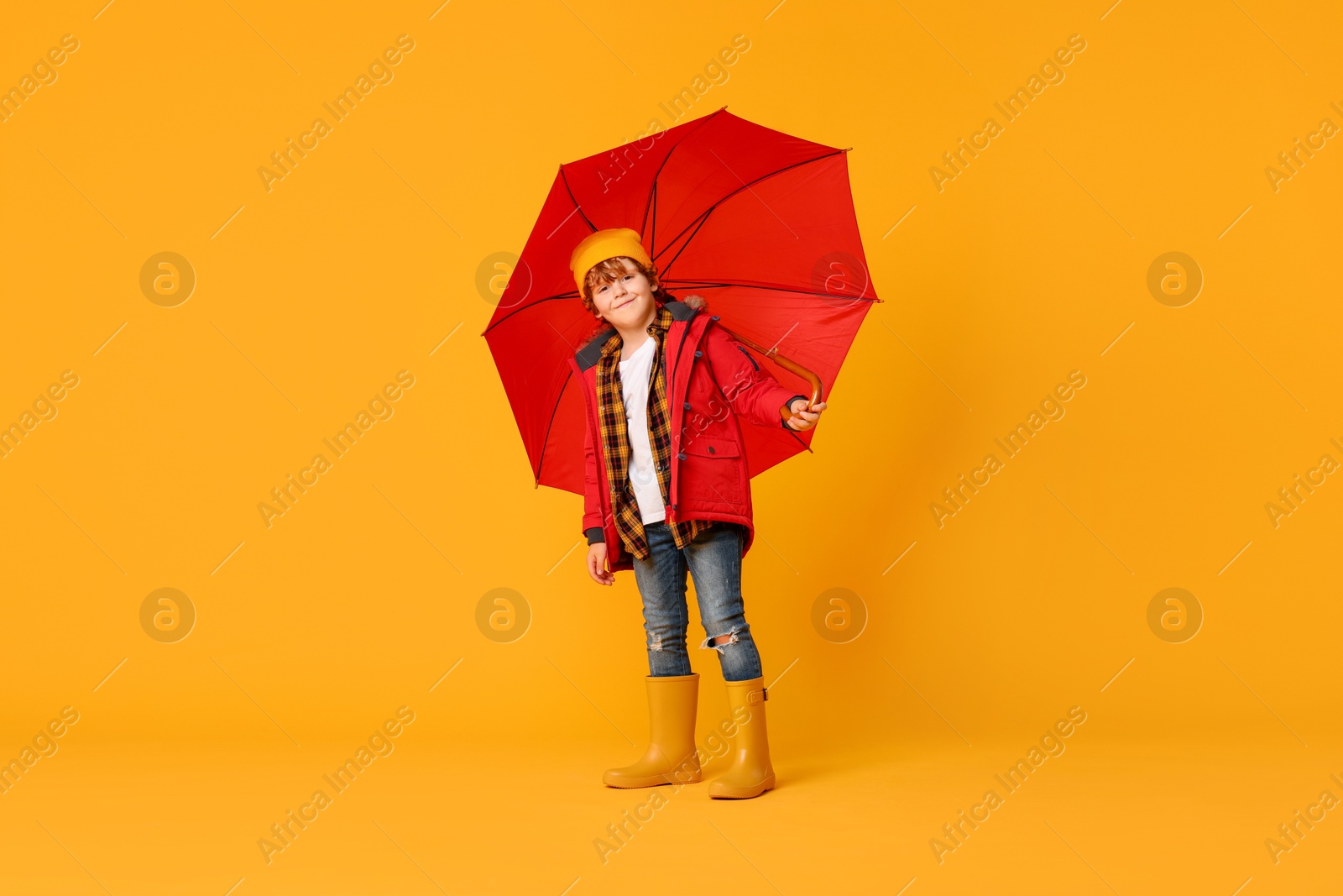 Photo of Little boy with red umbrella on orange background