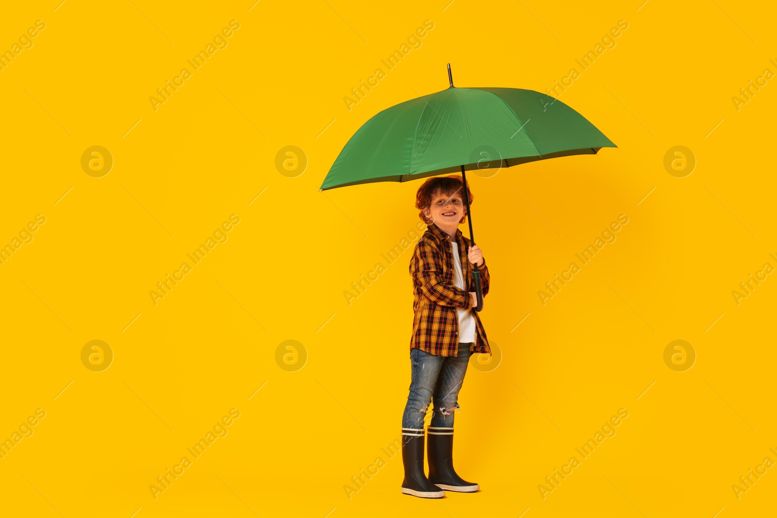 Photo of Little boy with green umbrella on orange background