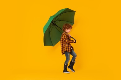 Photo of Little boy with green umbrella on orange background